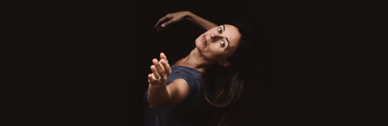 Anna Eklund tittar in i kameran, lutar sig bakåt och sträcker fram armen mot kameran.